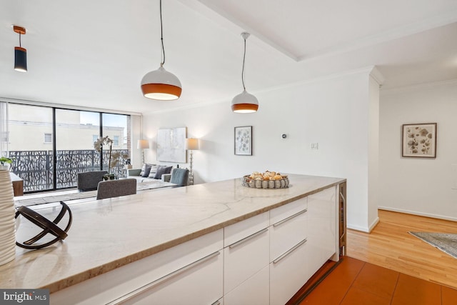 kitchen featuring hardwood / wood-style flooring, light stone counters, decorative light fixtures, crown molding, and white cabinets