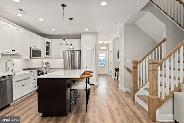 kitchen featuring white cabinets, a kitchen island, pendant lighting, light wood-type flooring, and appliances with stainless steel finishes