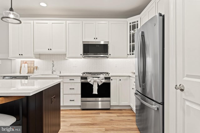 kitchen with pendant lighting, light wood-type flooring, appliances with stainless steel finishes, and white cabinets