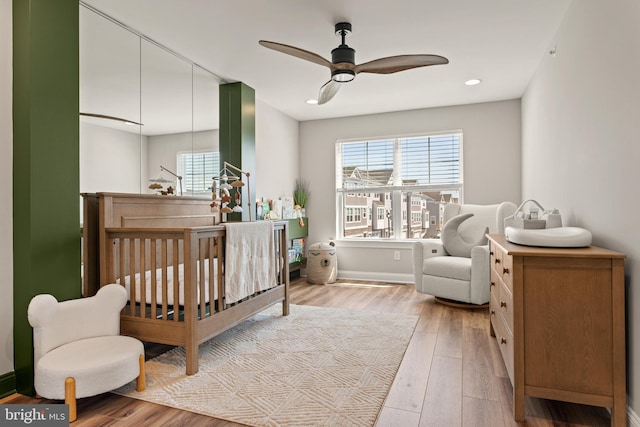 bedroom with light wood-type flooring, a nursery area, and ceiling fan