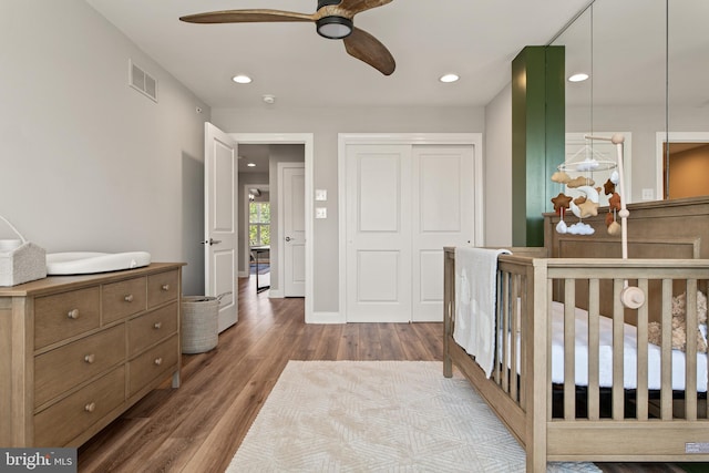 bedroom with a closet, wood-type flooring, ceiling fan, and a crib