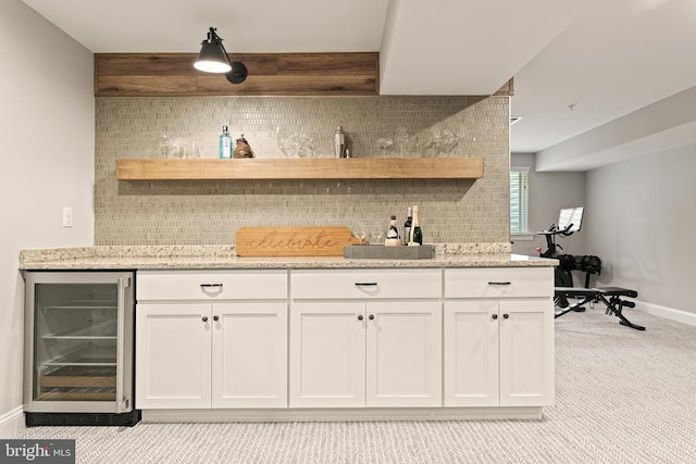 bar with wine cooler, white cabinetry, light carpet, light stone countertops, and decorative backsplash