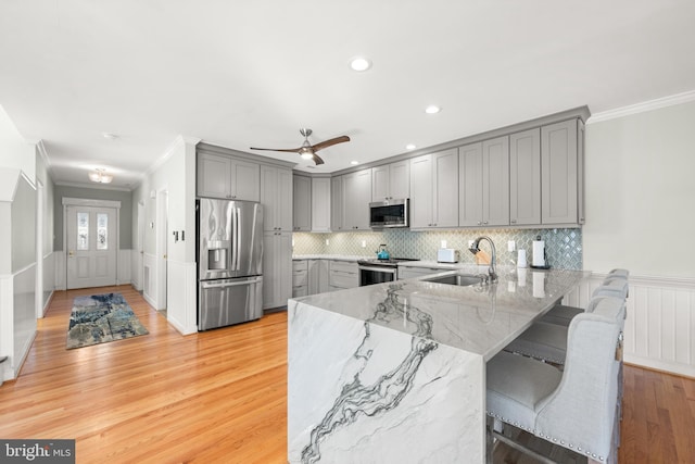 kitchen featuring kitchen peninsula, light stone countertops, light wood-type flooring, stainless steel appliances, and sink