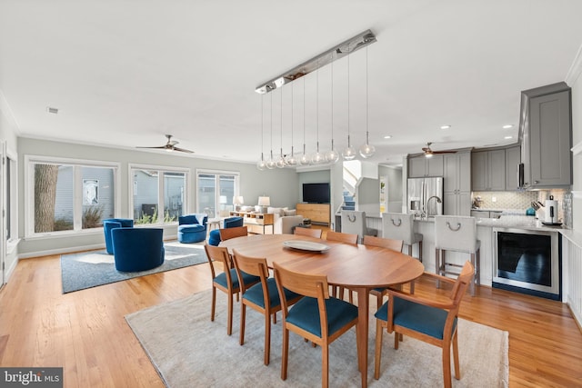 dining room with crown molding, ceiling fan, beverage cooler, and light hardwood / wood-style floors