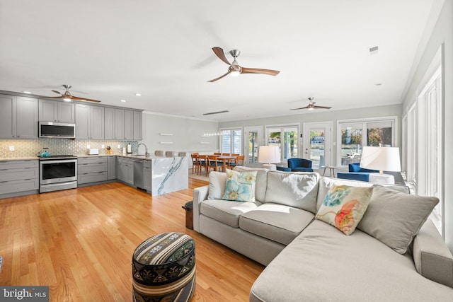 living room with light wood-type flooring, ceiling fan, crown molding, and sink