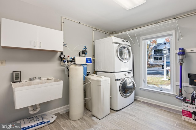 washroom with a wealth of natural light, light hardwood / wood-style flooring, stacked washer / drying machine, and sink