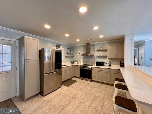 kitchen with stainless steel appliances, ornamental molding, wall chimney exhaust hood, decorative columns, and gray cabinetry