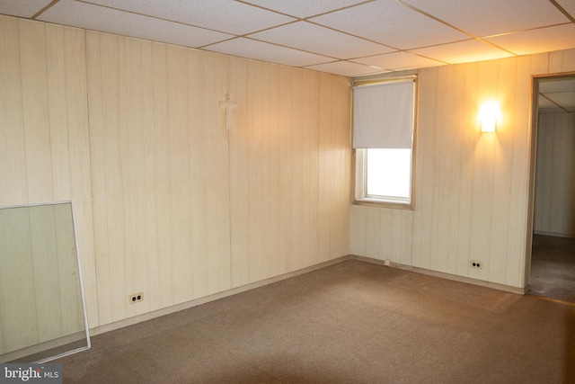 carpeted spare room featuring a drop ceiling and wooden walls