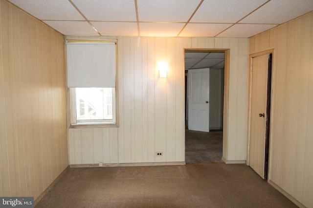 carpeted empty room featuring a paneled ceiling and wood walls