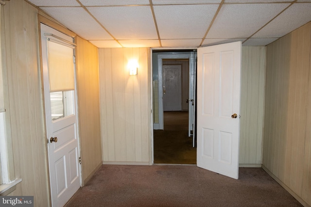 hall featuring carpet flooring, wood walls, and a drop ceiling