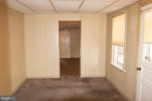 empty room with a drop ceiling, carpet floors, and wooden walls