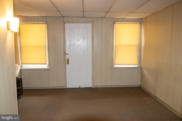 foyer entrance with a paneled ceiling, wood walls, and carpet floors