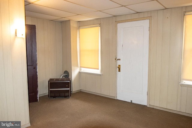 carpeted spare room with a paneled ceiling and wooden walls