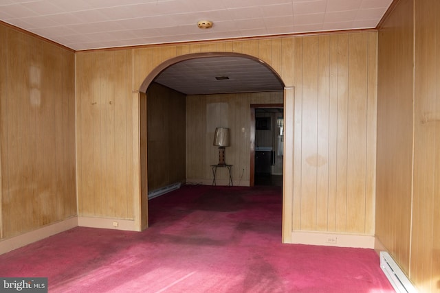 hallway with baseboard heating, wooden walls, and dark colored carpet