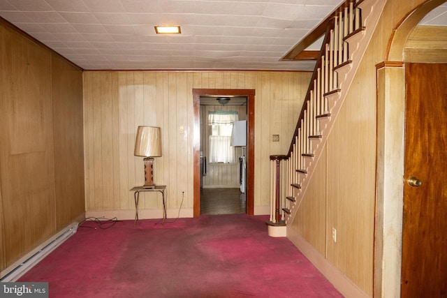 carpeted spare room featuring a baseboard radiator and wooden walls