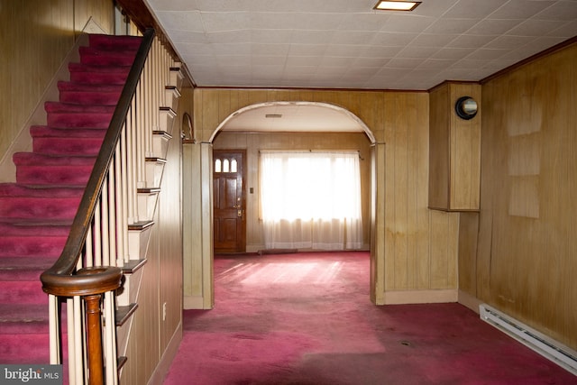 hall featuring baseboard heating, wooden walls, and carpet floors