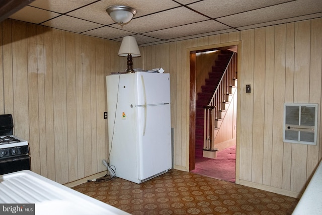 kitchen with white appliances, heating unit, a paneled ceiling, and wood walls