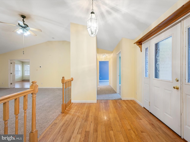 entrance foyer featuring ceiling fan with notable chandelier, a healthy amount of sunlight, vaulted ceiling, and light hardwood / wood-style floors