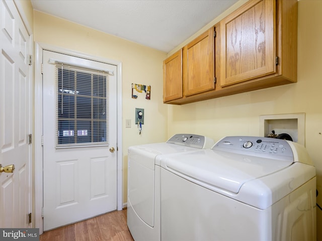 laundry room with cabinets, a textured ceiling, light hardwood / wood-style floors, and washing machine and clothes dryer