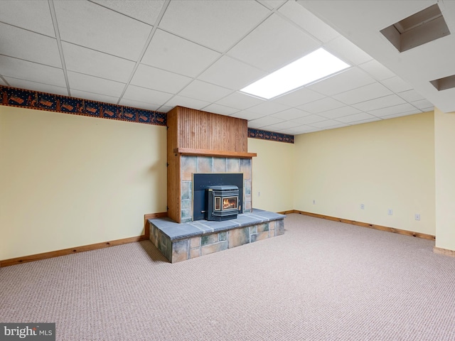 unfurnished living room featuring a paneled ceiling, a wood stove, and carpet floors