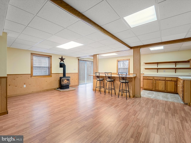 interior space with a drop ceiling, light hardwood / wood-style floors, a wood stove, and a wealth of natural light