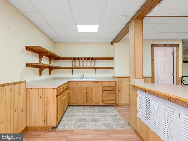 kitchen featuring a paneled ceiling, light wood-type flooring, sink, and wooden walls