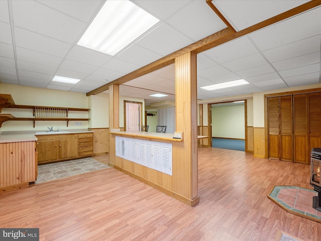 kitchen with a wood stove, light hardwood / wood-style flooring, a drop ceiling, and wooden walls