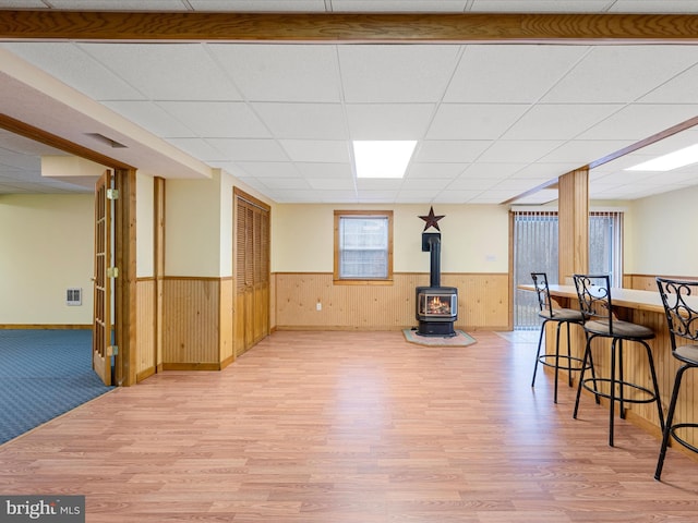 interior space featuring a paneled ceiling, wood walls, light wood-type flooring, and a wood stove