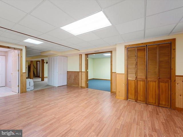 basement featuring a paneled ceiling, wooden walls, and light wood-type flooring