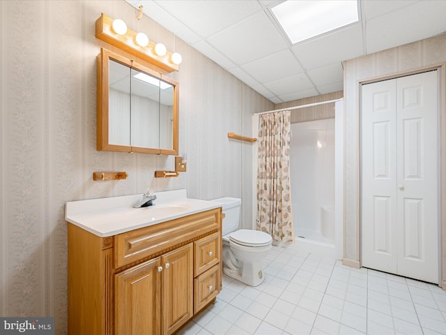 bathroom with a paneled ceiling, vanity, tile patterned floors, toilet, and walk in shower