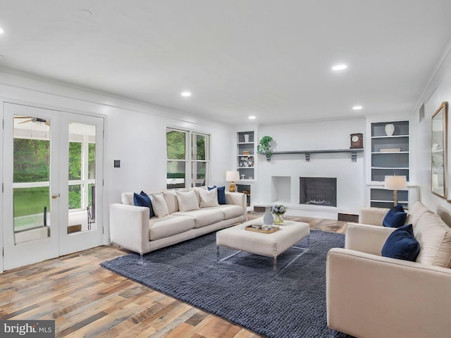 living room with built in shelves, hardwood / wood-style flooring, crown molding, and french doors