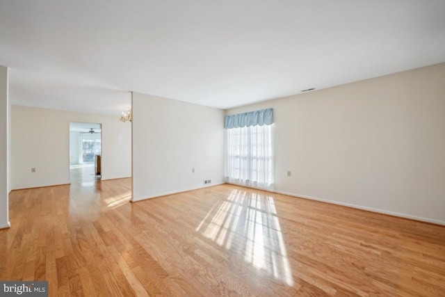 unfurnished room featuring ceiling fan with notable chandelier and light wood-type flooring