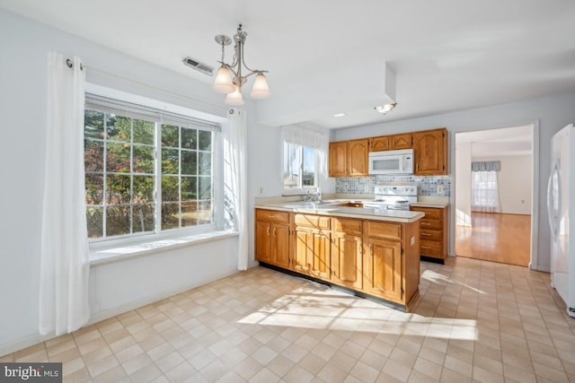 kitchen featuring decorative backsplash, kitchen peninsula, white appliances, pendant lighting, and a chandelier