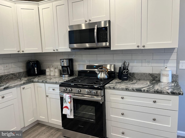 kitchen featuring dark stone counters, decorative backsplash, white cabinetry, light wood-type flooring, and appliances with stainless steel finishes