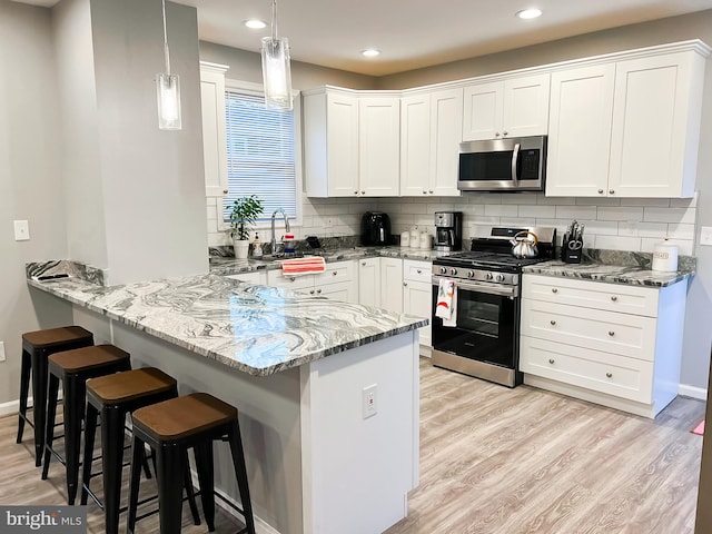 kitchen featuring kitchen peninsula, white cabinets, hanging light fixtures, and stainless steel appliances