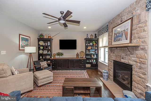 living room with ceiling fan, a stone fireplace, and dark wood-type flooring