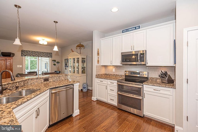 kitchen featuring appliances with stainless steel finishes, dark wood-type flooring, sink, decorative light fixtures, and white cabinetry