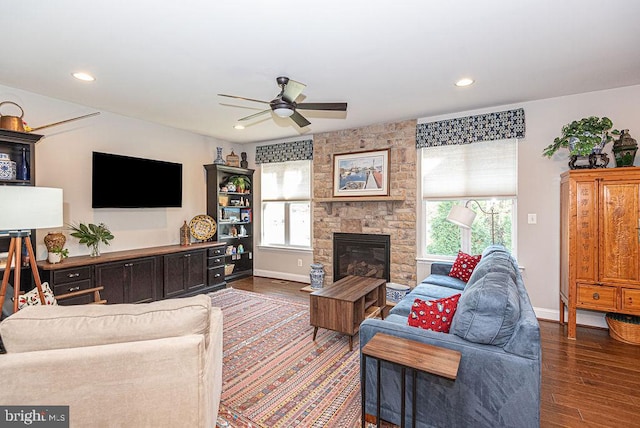 living room with dark hardwood / wood-style floors, a stone fireplace, ceiling fan, and a healthy amount of sunlight