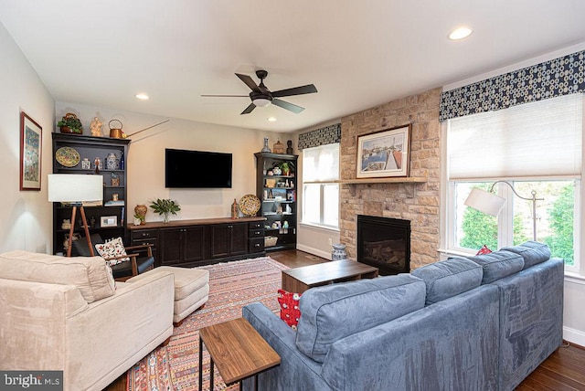 living room featuring a stone fireplace, ceiling fan, and dark wood-type flooring