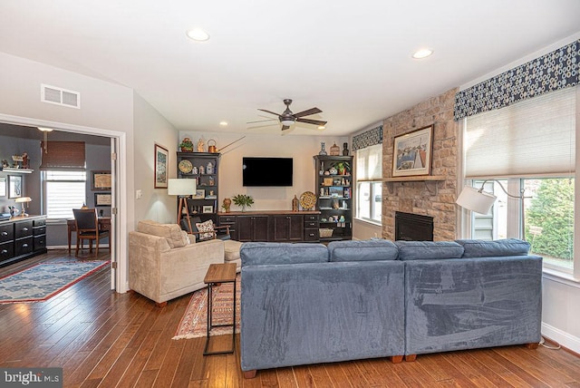 living room featuring ceiling fan, a healthy amount of sunlight, dark hardwood / wood-style flooring, and a fireplace