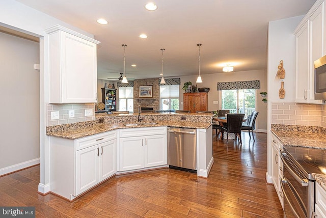 kitchen featuring kitchen peninsula, appliances with stainless steel finishes, hardwood / wood-style flooring, decorative light fixtures, and white cabinetry