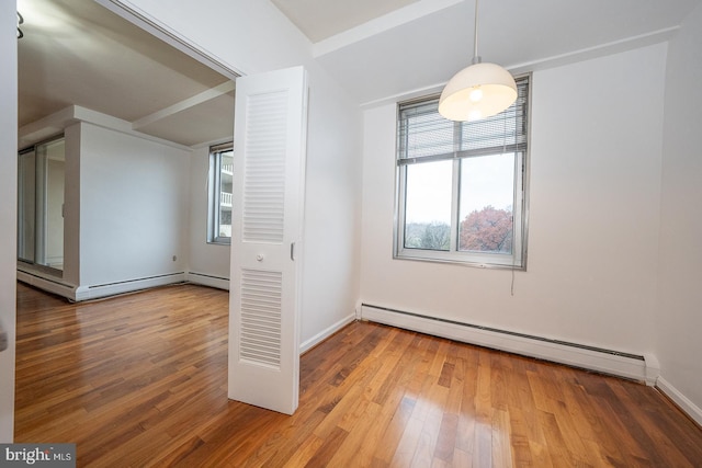unfurnished bedroom with baseboard heating, wood finished floors, a baseboard heating unit, and baseboards