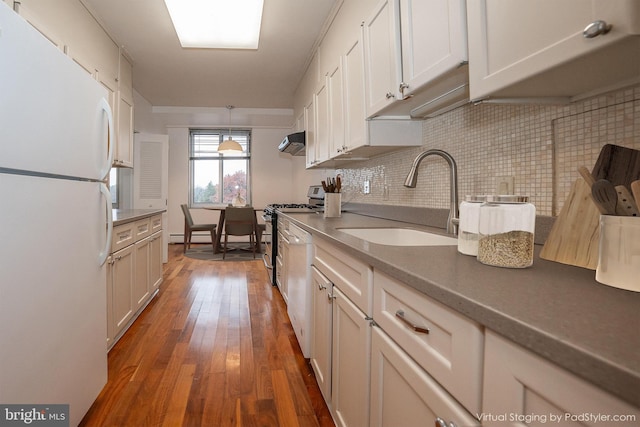 kitchen with white appliances, a sink, under cabinet range hood, tasteful backsplash, and hardwood / wood-style flooring