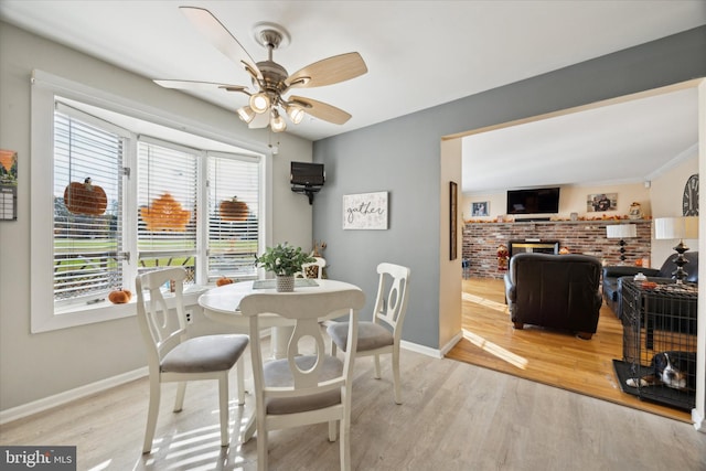 dining room with a brick fireplace, ceiling fan, and light wood-type flooring