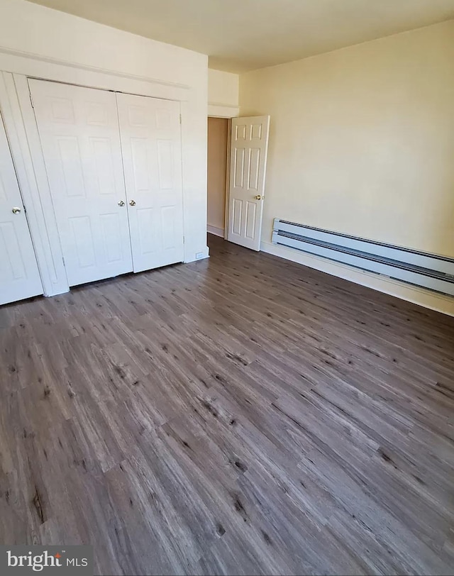 unfurnished bedroom with dark hardwood / wood-style flooring, a closet, and a baseboard heating unit