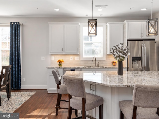 kitchen with pendant lighting, stainless steel refrigerator with ice dispenser, white cabinetry, and sink