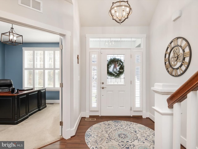 entrance foyer with a wealth of natural light, a chandelier, vaulted ceiling, and dark hardwood / wood-style flooring