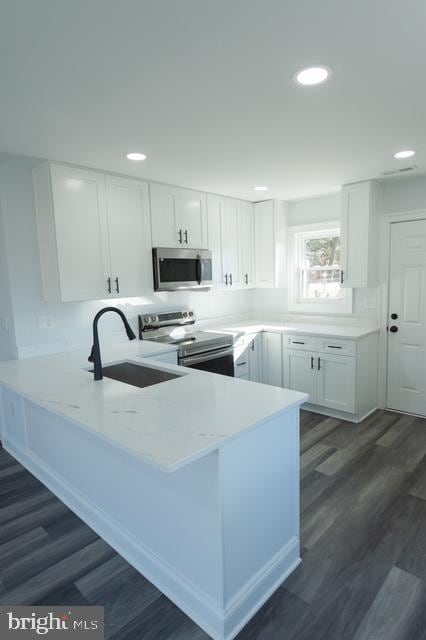 kitchen with sink, kitchen peninsula, dark hardwood / wood-style flooring, white cabinetry, and stainless steel appliances