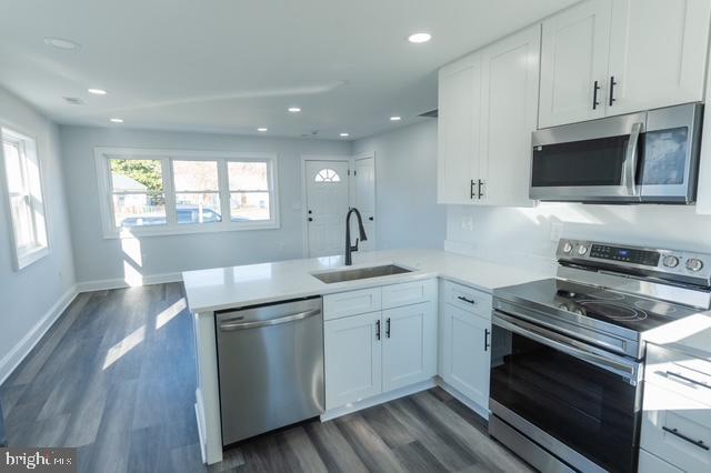 kitchen with sink, stainless steel appliances, dark wood-type flooring, kitchen peninsula, and white cabinets