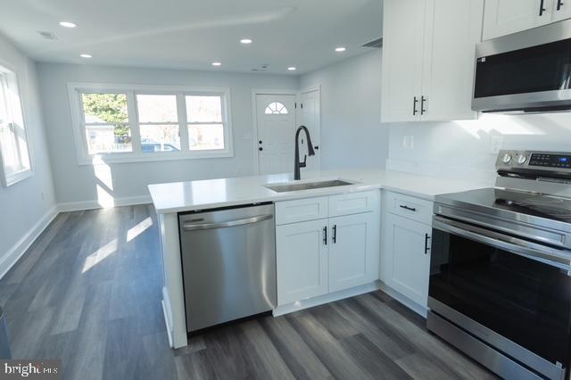 kitchen with kitchen peninsula, appliances with stainless steel finishes, dark wood-type flooring, sink, and white cabinetry